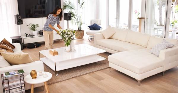 A lady water flower in her Livingroom. There is a soft set in beige