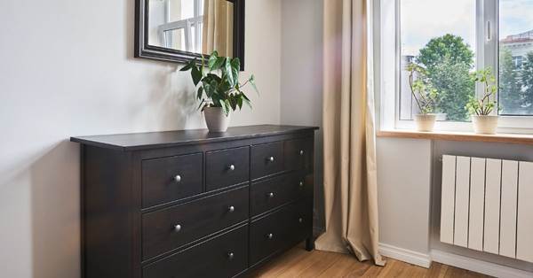 On the corner of a dark brown living room dresser, there is a small plant on top.